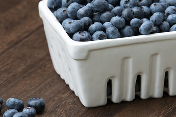 A white ceramic berry basket filled with fresh blueberries on a wooden table