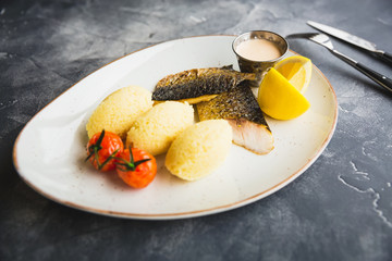 Delicious dish with grilled fish, millet porridge, tomato, lemon slice and shrimp sauce. Tasty food in restaurant