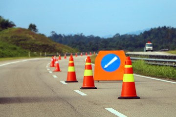 Traffic cones and a sign with a white arrow on highway as warning sign for road user