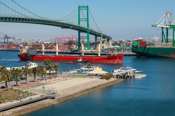 Worldwide Supply Chain, A Red Bulk Carrier Entering the Port of San Pedro at Vincent Thomas Bridge and Container Ships Unloading in Los Angeles California Shipping Port