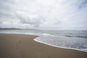 Overcast ocean beach. Shallow waves. Coastal line on background.