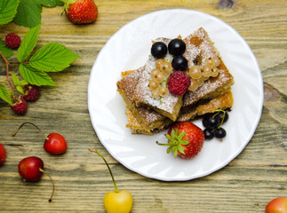 pieces of cake with berries and fresh strawberry currant and cherry berries on wooden background