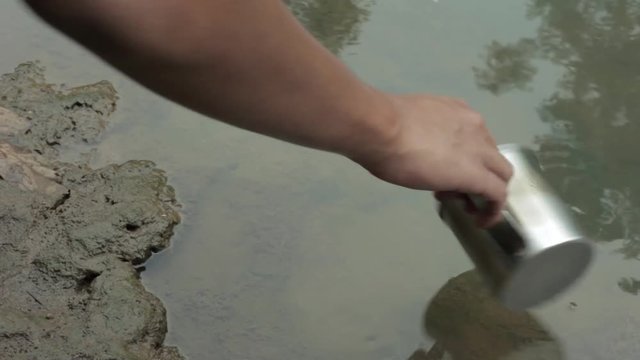 Scooping dirty water from river with metal mug