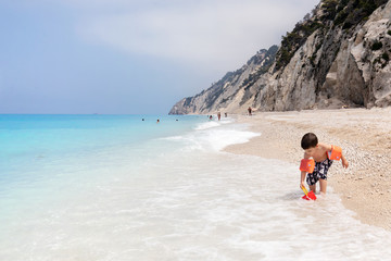 Young boy playing with sand and water at Egremni beach, Lefkada, Greece