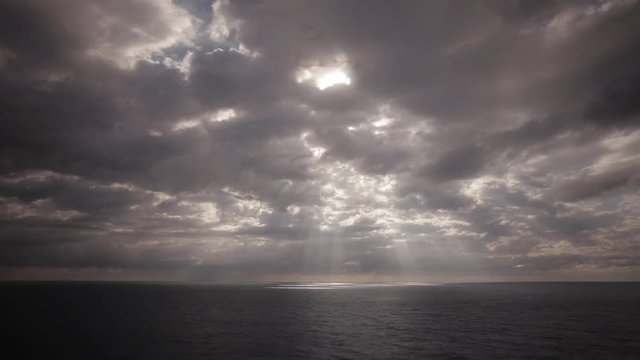 Time lapse of beautiful clouds over the ocean with golden sun rays arching out