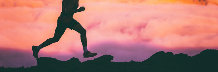 Trail runner legs of man athlete running on rocks in sky pink clouds background. Panoramic banner...
