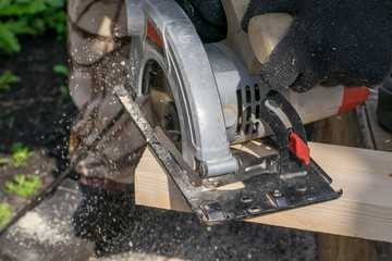 a man sawing a Board with a power tool, chips fly in all directions. Construction, wood processing