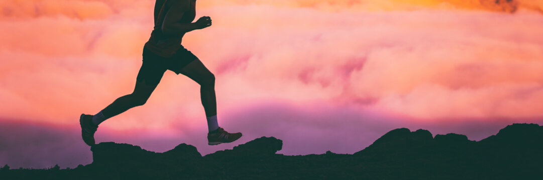 Trail runner legs of man athlete running on rocks in sky pink clouds background. Panoramic banner silhouette of run workout fitness concept.