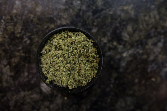 Marijuana grinder - isolated - space for text - with freshly ground marijuana inside - on a grey background