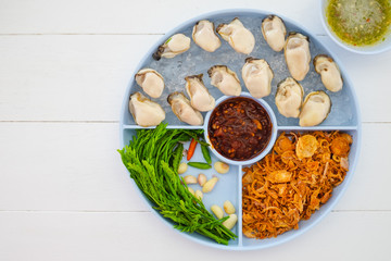 Oysters food and chili sauce, red onion fried Thai cuisine style on white wooden table background with copy space.