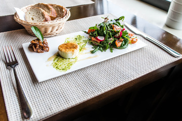 Healthy vegetable summer salad, fresh vegetables and dressing with grilled cheese flambe arranged on plate dinner table