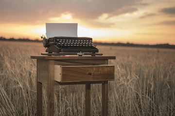 typewriter on a walnut bedside table in a wheat field at sunset