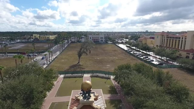 This is another pull away drone shot of a lake front park plaza. The center of attention is the bell tower in the park as the drone pulls away over the lake that it surrounds.