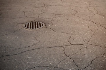 Cast iron metal rain manhole cover in old asphalt with a lot of cracks.