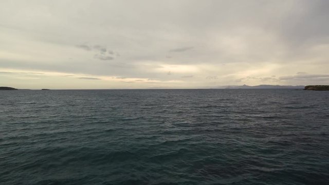 Flying over the sea on a cloudy day. Small island on the horizon.