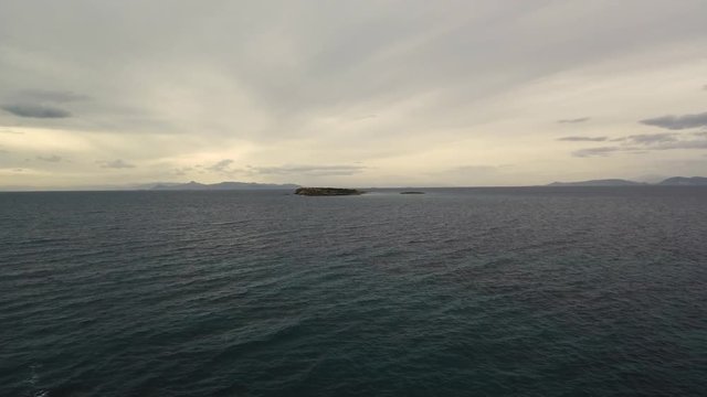 Flying over the sea on a cloudy day. Small island on the horizon.