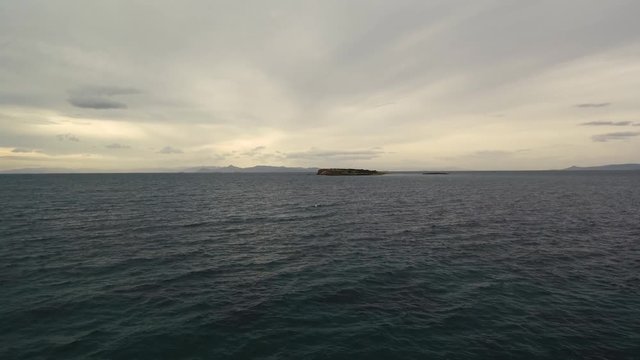 Flying over the sea on a cloudy day. Small island on the horizon.