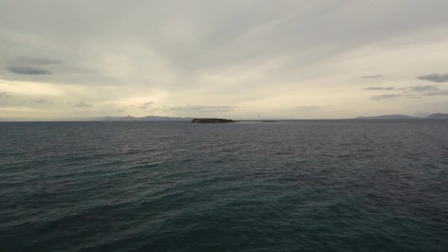 Flying over the sea on a cloudy day. Small island on the horizon.