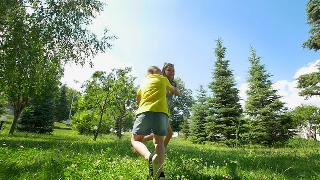 Cute little boy runs away from his happy sister through the spruce trees at sunny day