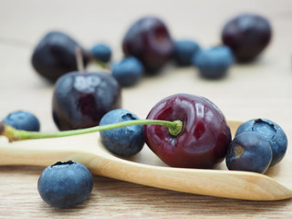 Fresh cherry and blueberry with spoon on wooden background. Healthy food and diet.