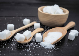 Wooden bowl and spoon with sugar cube on dark wood background.