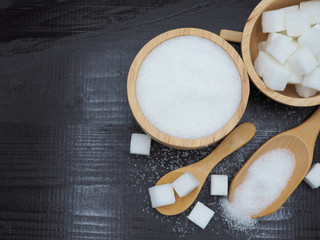 Wooden bowl and spoon with sugar cube on dark wood background.