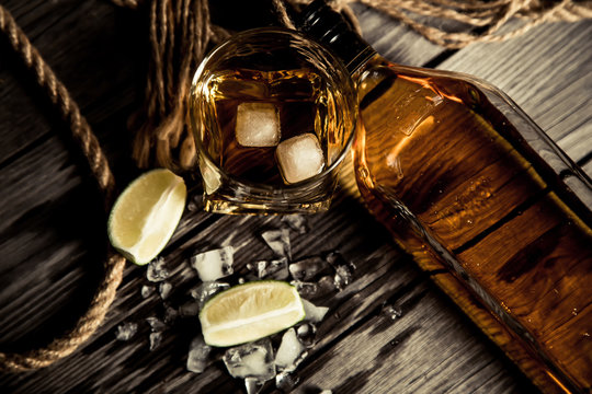 bottle of rum whiskey bourbon and a glass with ice on a wooden background