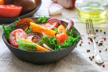 Delicious summer salad of colorful (yellow, red and black) ripe tomatoes, red onions and lettuce with spices. Healthy dinner or lunch