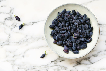 Fresh ripe honeysuckle berries in a ceramic bowl on a grey marble table