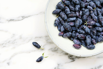 Fresh ripe honeysuckle berries in a ceramic bowl on a grey marble table