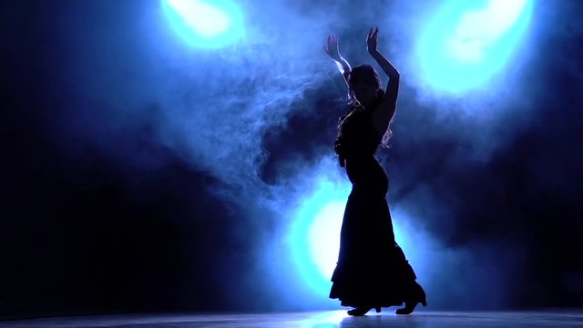Flamenco. Dancer in the dark room performs elegant movements with her hands . Llight from behind. Smoke background. Silhouette. Slow motion