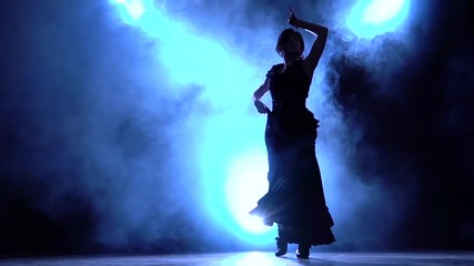 Dancer in a chic dress in an incendiary dance of flamenco . Llight from behind. Smoke background. Silhouette. Slow motion