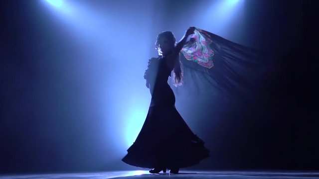 Flamenco. Girl is dancing with a manton in the hands of a Spanish incendiary dance. Llight from behind. Smoke background. Silhouette. Slow motion