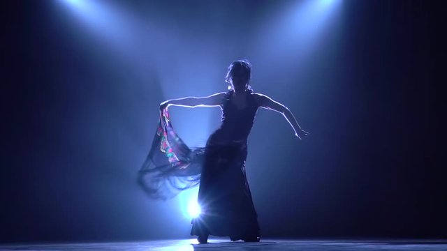 Flamenco. Woman is dancing with a manton in the hands of a Spanish incendiary dance. Llight from behind. Smoke background. Silhouette. Slow motion