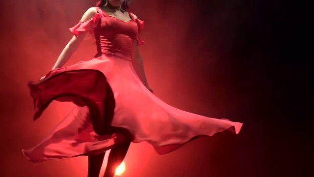 Dancer in a chic dress turns in an incendiary dance of Argentine flamenco . Llight from behind. Smoke background. Slow motion.