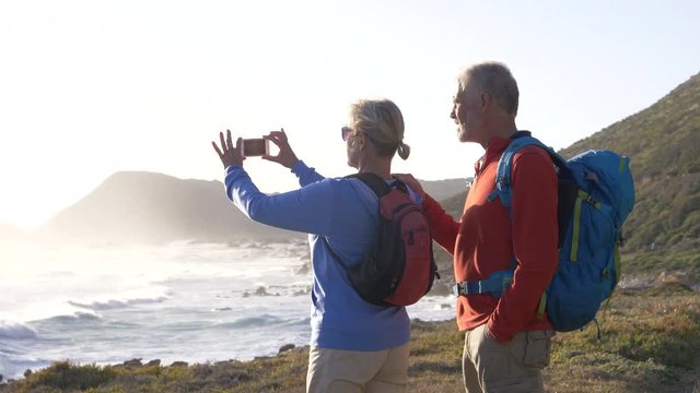 Mature hikers stopping to take photos overlooking the sea