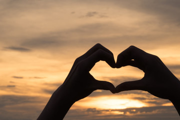 Hands as heart shape with beautiful sky in warm color twilight sunset background,love and romantic concept.