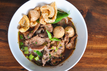 Noodle Soup Thai Style (Pork or Beef)) with crackling in white bowl on blown wooden table background.