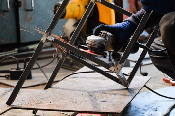 Technician industrial worker use grinder steel cutting create metal steel chair. Flash burn, ultraviolet light, sparks, infrared light effect, He use welding mask to protect eyes. Industry concept.