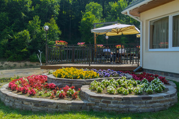 Three-level flowerbed with red, yellow, blue and white flowers near the street terrace of the cafe