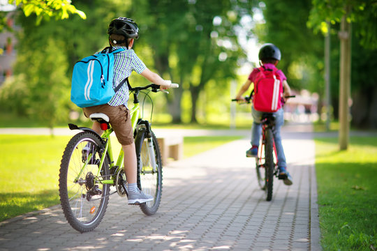 Children with rucksacks riding on bikes in the park near school. Pupils with backpacks outdoors