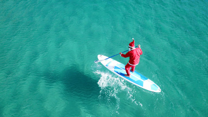 Aerial drone of Santa Claus paddle surfing in Australian emerald clear sea waters - Powered by Adobe