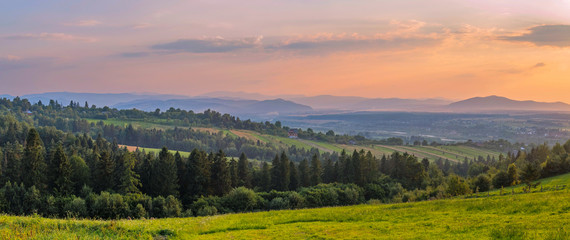 Elegant panorama of the mountainous terrain with valleys forest planting beautiful peaks in the distance against the background of the evening sky.