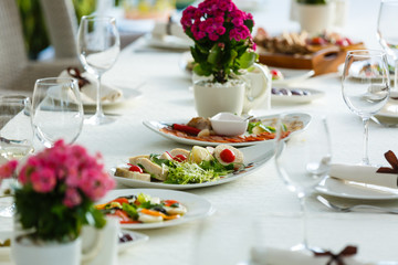 Table served for special occasion. Empty plate, glasses, forks, napkin and flowers on table covered with white tableclothes. Elegant dinner table. White table setting