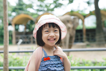 Cute little girl watching animals at the zoo on warm and sunny summer day. Children watching zoo animals through the window. Family time at zoo.