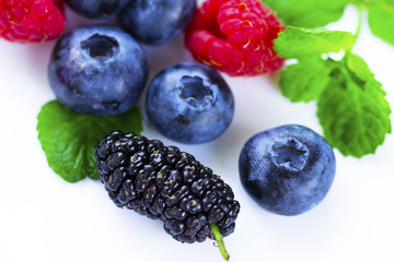 Close-up arrangement mixed, assorted berries including blackberries, strawberry, blueberry, raspberries and fresh leaf on white