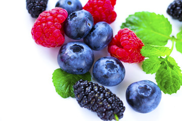 Close-up arrangement mixed, assorted berries including blackberries, strawberry, blueberry, raspberries and fresh leaf on white