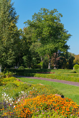 Plakat Beautiful summer day landscape in the park. Flowerbeds with flowers green lawn in the shade of green trees.