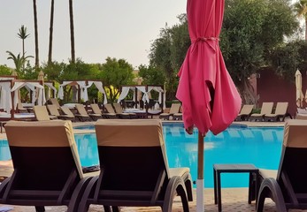 Transats en résine tressée, parasols et lits à baldaquin au bord d'une piscine d'hôtel