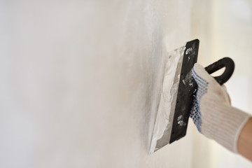 Spatula with putty in hand. Worker puts of plaster on wall.